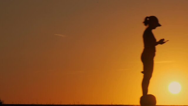 Silhouette of girl rides on segway on road on background of sun.