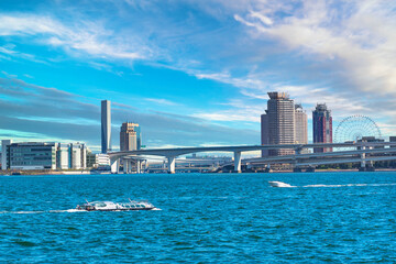 Obraz premium Water buses sailing on Tokyo Bay in front of the double-layered expressway of Rainbow Bridge with the buildings and ferris wheel of Odaiba and Ariake islands in the back.