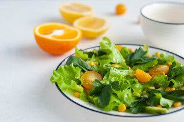 Summer salad with corn, avocado, leaf basil salad and citrus sauce. Orange, lemon and yellow tomatoes next to the plate.