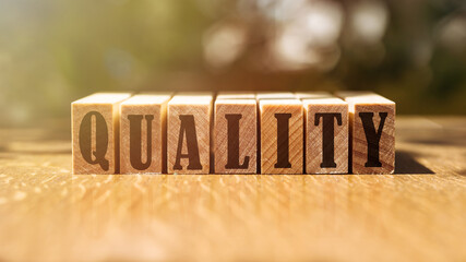 Quality word made with building wooden blocks on table in sunlight. concept