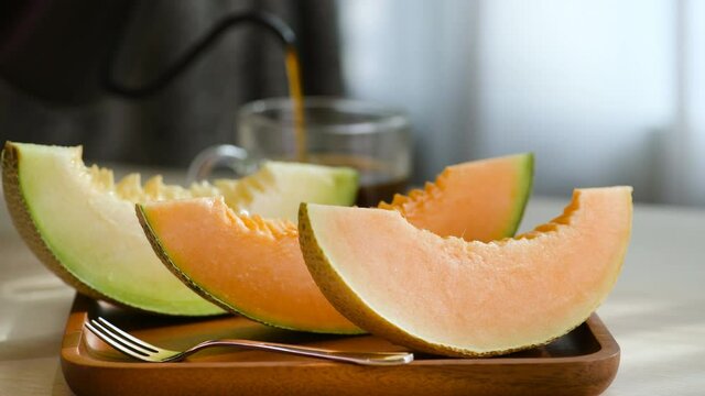 Slice pieces of sweet green orange melon for fruit dessert with Coffee break at rest time after work at home. Pouring hot black coffee in empty glass cup and eat melon in sunlight time from window. 