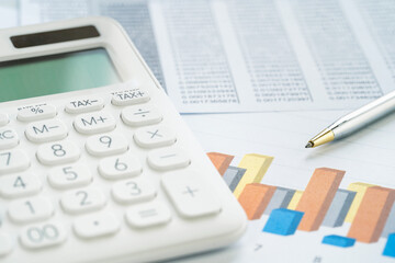 Finance and business concept. White calculator on financial graphs on office desk, paperwork binder, glasses. Accounting budgeting or market analysis. Web banner with copy space. Minimal