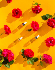Three cosmetic glass bottles  for essential oils with roses on a yellow background. Spa still life with Natural Serums in glass bottle. Dropper Bottle Mock-Up