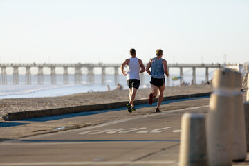 Men running at the beach near a beach pier.