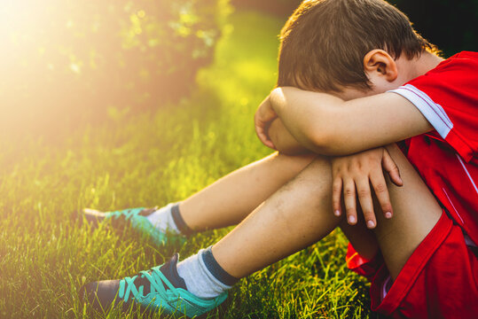 Tired boy after sport. A boy dressed in sports attire sits on the grass tired after playing football.