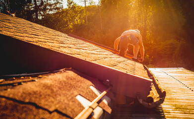 The man is repairing the roof. The worker cuts the sheet for roof renovation, laying tiles.