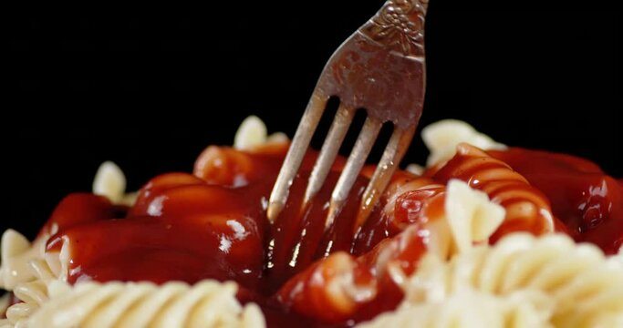 Boiled pasta fusilli mixed with tomato sauce with a fork.