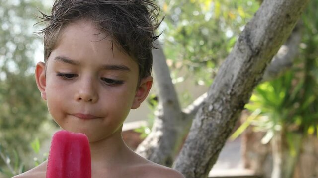 Video in 4 k di un bambino biondo che si gusta un ghiacciolo alla frutta  nel giardino di casa