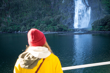 A female tourist on a cruise boat watching a beautiful waterfall in Milford Sound, New Zealand