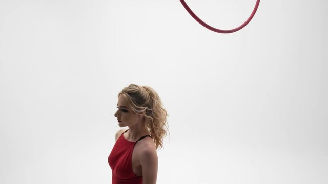 Flexible pretty blonde girl in a red dress and black
stockings performs acrobatic elements in an air hoop,
white cyclorama location.