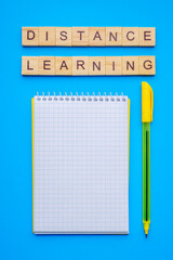 Wooden letter cubes with phrase distance learning, notepad and pen on blue background. possibility of continuing distance learning creative concept