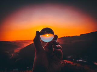 Taking photos of sunset through the small glass ball holding in hand