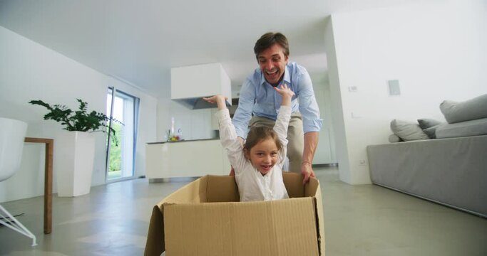 Authentic shot of carefree happy smiling father and daughter are having fun to racing with empty box just moved into a new house.