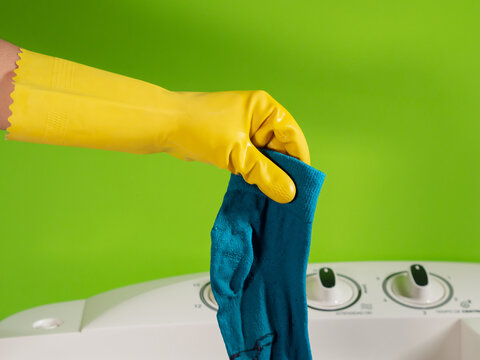 gloved hands washing a blue sock and green background