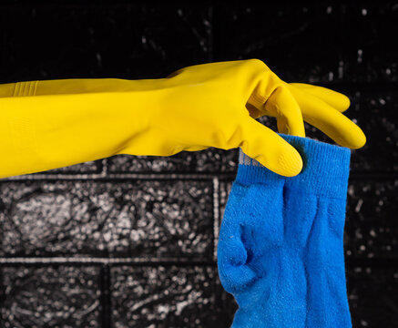 gloved hand holding a blue sock and textured black brick background
