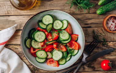 Healthy vegetable salad of fresh tomato, cucumber, dill and spices and oil in bowl on rustic wooden background. Diet concept.
