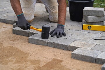 A craftsman lays concrete paving stone blocks on sand. Paving stone work.