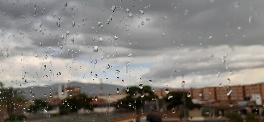 Una ventana con gotas de agua. Y en el fondo un paisaje de la ciudad y un cielo nublado después de...