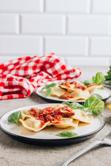 Italian ravioli with meat tomato sauce and basil leaves with on a white dishes on concrete background.