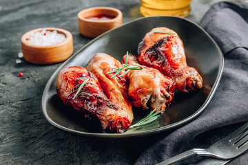 Chicken legs on black plate with red sauce and rosemary on black rustic background.