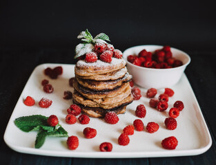 Chocolate pancakes with fresh raspberries and mint on black background