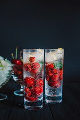Cold lemonade with raspberries, lemon, ice and cherries on black background