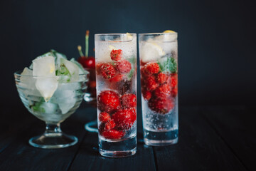 Cold lemonade with raspberries, lemon, ice and cherries on black background