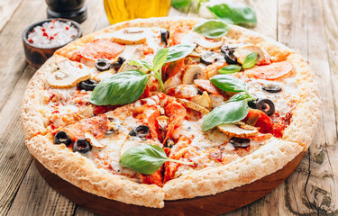 Sliced italian pizza with salami, mozzarella, mushroom, tomatoes, black olives and basil leaves on...