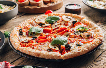 Sliced italian pizza with salami, mozzarella, mushroom, tomatoes, black olives and basil leaves on wooden background. Italian traditional food. Popular street food concept