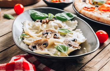 Italian cuisine - ravioli pasta with champignon mushrooms and parmesan cheese on black plate on wooden background.