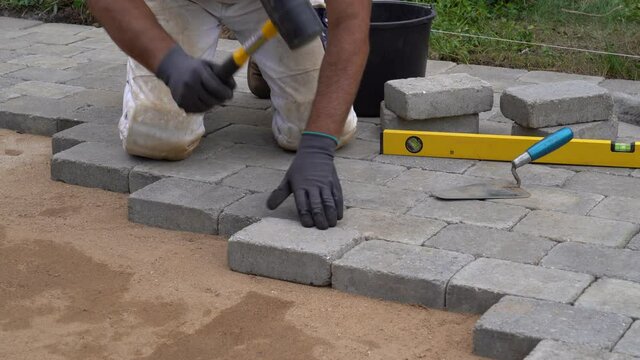 A craftsman lays concrete paving stone blocks on sand. Paving stone work. 