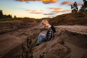 Fototapeta na wymiar Young boy sitting on sandy bank at dusk
