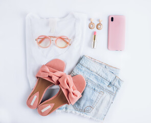 Female clothes and accessories with white t-shirt, jeans, sunglasses, lipstick, pink shoes, earrings headphones, straw hat and smartphone on white background