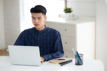 Young business man working from home with laptop computer on desk, freelance male sitting stay home using notebook for communication and relax on table, entrepreneur in startup business, new normal.