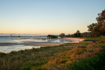 Sunset glow at the beach, with evening glow on the grassy foreshore, sandy beach, birds, and boats moored in the distance. Dunwich, North Stradbroke Island, Moreton Bay, Queensland, Australia.