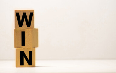 Three wooden cubes with word WIN, on white table, more in background, space for text in right down corner