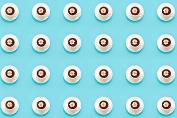 Pattern made from white cup of tea with chamomile on dish saucer, blue background. Top view Flat lay