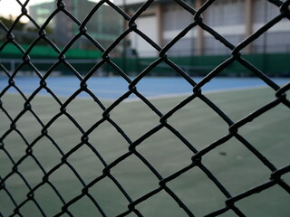 closeup of metal fence with blurred tennis court background.