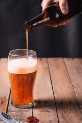 waiter serving craft beer in a glass bottle on a rustic wooden table and dark environment.