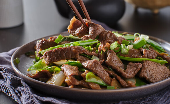 eating chinese beef and snowpeas stirfry on plate with chopsticks