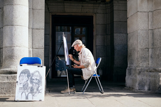 Old Male Street Painter Drawing Portrait Of Tourist - Powered by Adobe