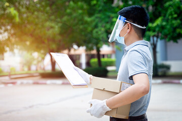 Delivery man employee in face mask and shield delivers parcels and box post to customer order online shopping during COVID-19 pandemic.