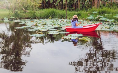 Fototapeta na wymiar Asian woman rowing a small boat in the Lotus pond at garden with green tree background.