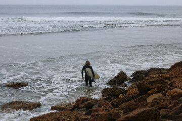 a young surfer walking along the rocky shore with his surfboard looking for a place to join the surf, coastal Victoria, great ocean road, Australia