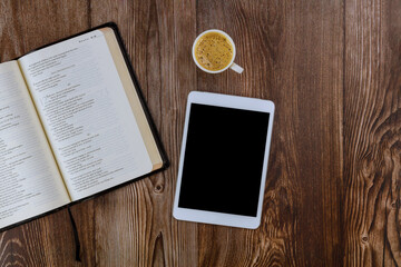 Open Holy Bible lying on wooden table in a reading the digital tablet with cup of coffee
