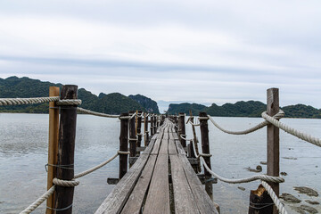 Fototapeta premium A long old wooden bridge rests in to the sea with tree.