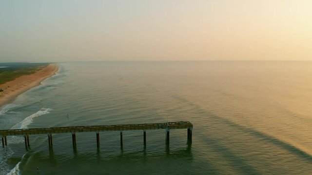 Saharan dust sunrise with aerial view of a pier at the beach.