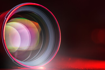 The camera lens with red light. Close-up of the camera lens on a black background with red illumination. Optics.