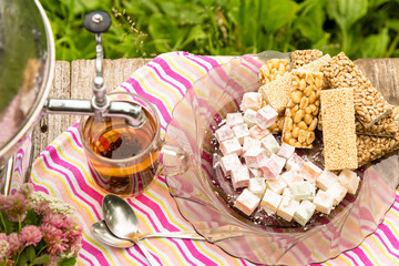 Oriental sweets and a Cup of tea with a samovar tap on the background of green grass.