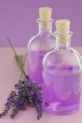 Obraz na płótnie Canvas Lavender water. Lavender Extract.Lavender essence in transparent bottles set and sprigs of lavender flowers on a combined pink-purple background.Organic natural cosmetics concept. Lavender cosmetics